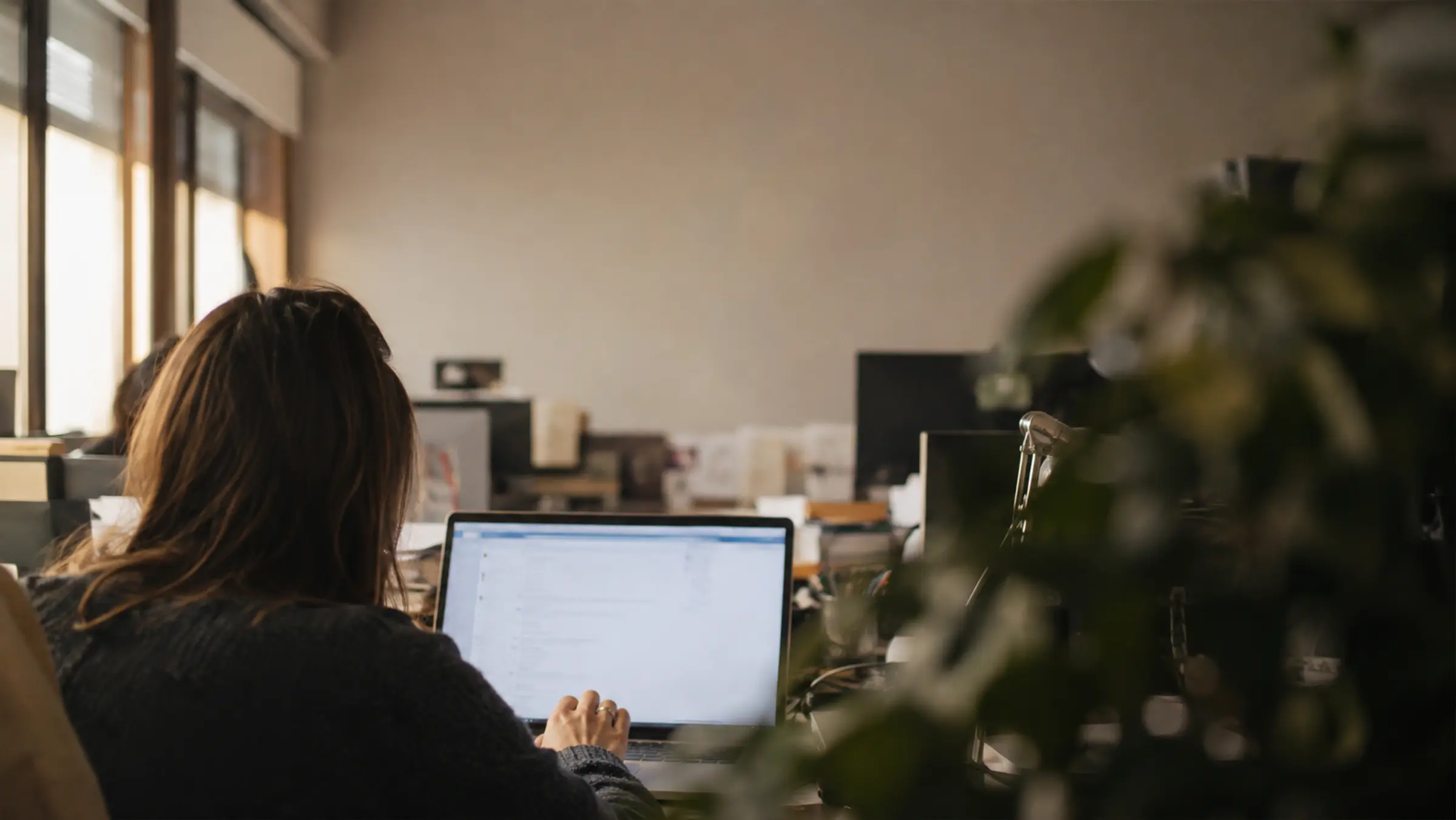 Une collaboratrice travaille sur son ordinateur portable dans un bureau clair, éclairé par la fenêtre